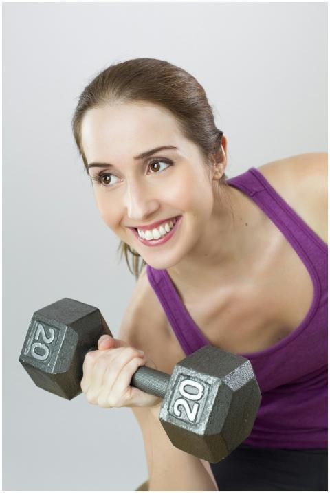 Young woman exercises with 20 lb dumbbell, showing