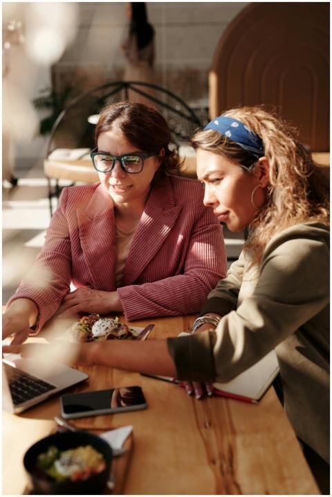Two women engaged in teamwork at a café table, usi
