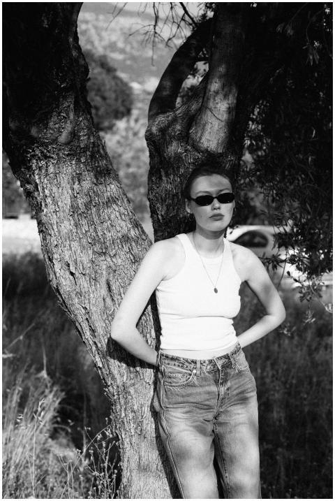 Chic woman in sunglasses leaning against a tree, s