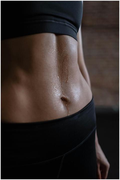 A close-up of a fit woman's toned abdomen with swe