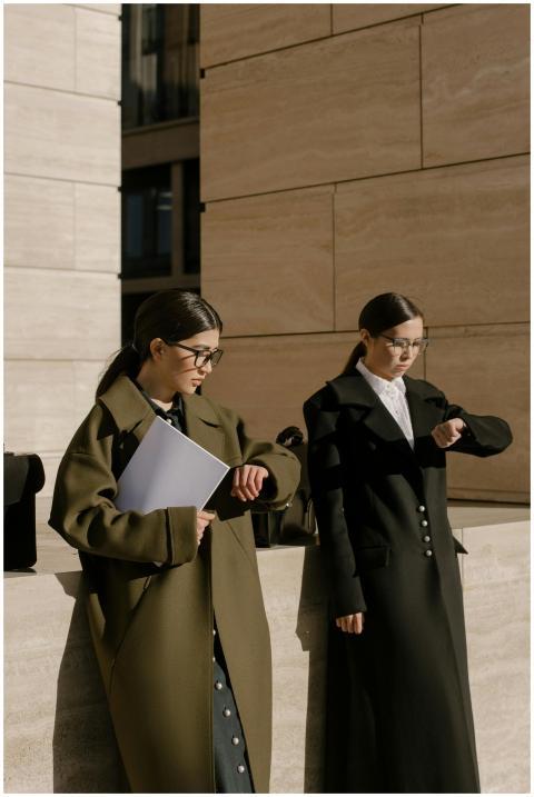 Two fashionable women in long coats checking time