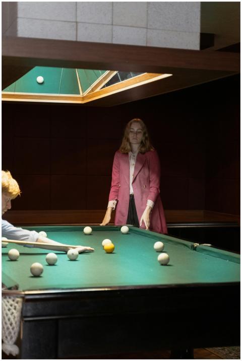 A woman in a pink jacket plays billiards indoors.