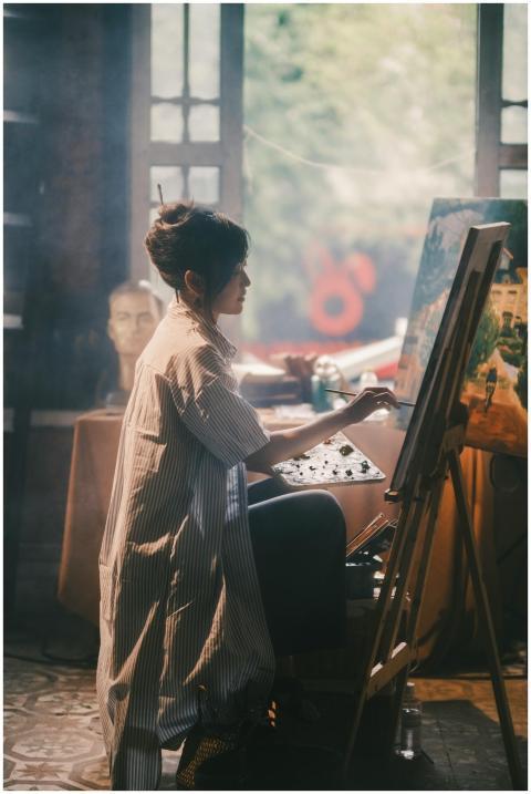 Asian woman painting at an easel in a soft-lit art