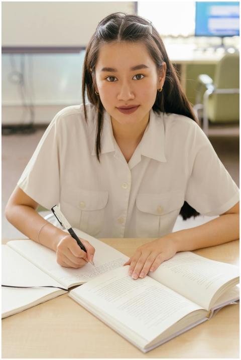 A focused young woman in a library writing in a no