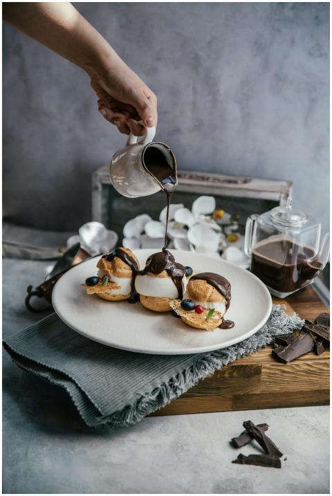 Profiteroles topped with chocolate sauce being pou