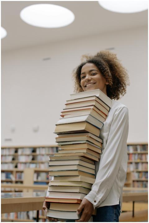 Smiling woman with a large stack of books in a bri