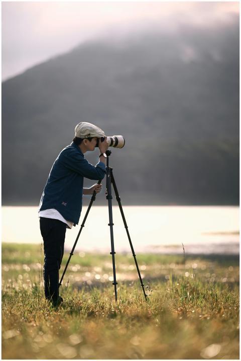 A young adult photographer using a tripod in a sce
