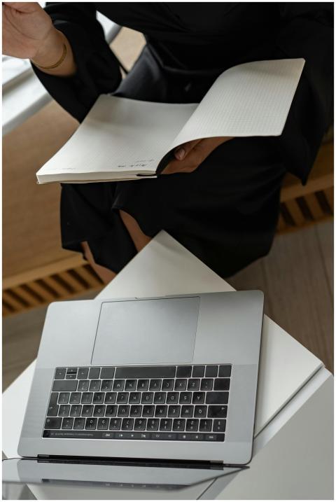 A woman multitasks with a laptop and notebook, sym