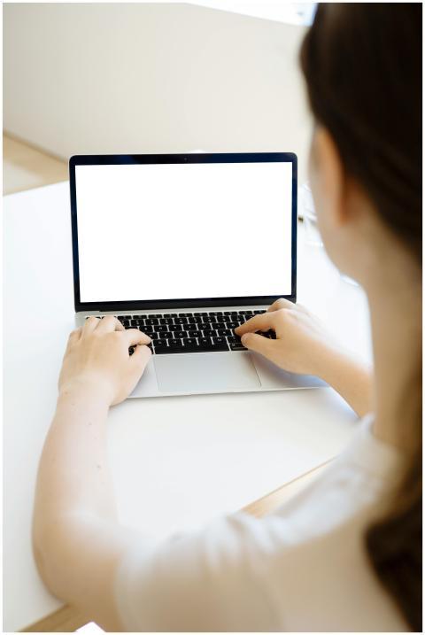A woman typing on a laptop with a blank screen, id