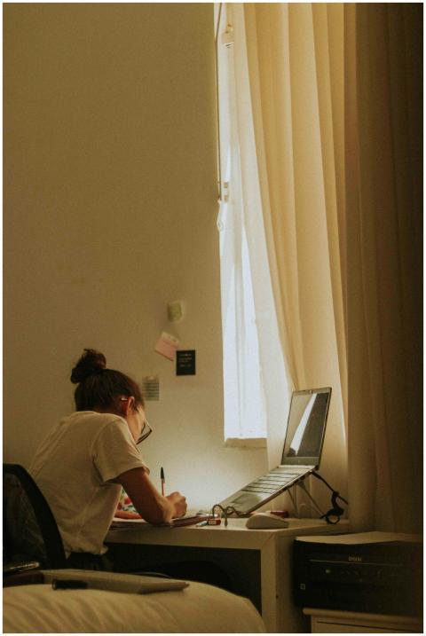 A young woman writing at a desk by a window, bathe