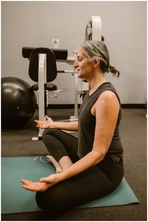 Elderly woman meditating on mat in gym, focusing o