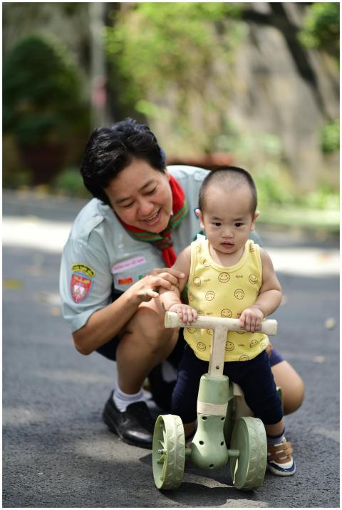 Child riding a tricycle supported by an adult in a