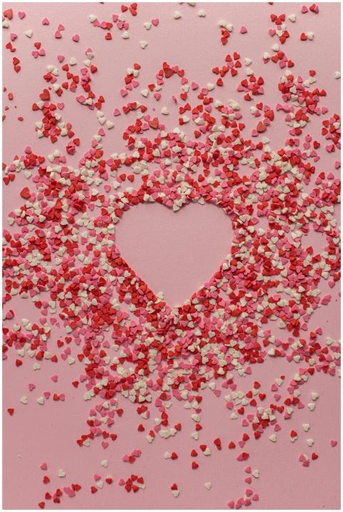 Heart-shaped confetti arrangement on a pink backgr