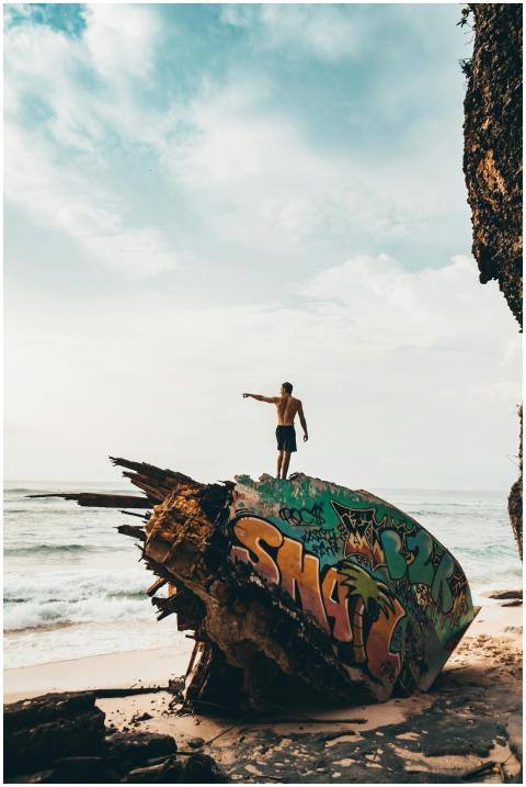 A man stands atop a graffiti-painted shipwreck on