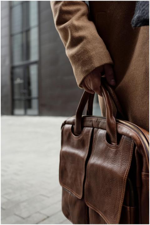 A person holding a brown leather bag, showcasing f