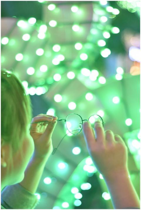 A young woman holds eyeglasses amidst defocused gr