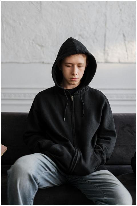 Teenager in a black hoodie sitting on a couch, ref