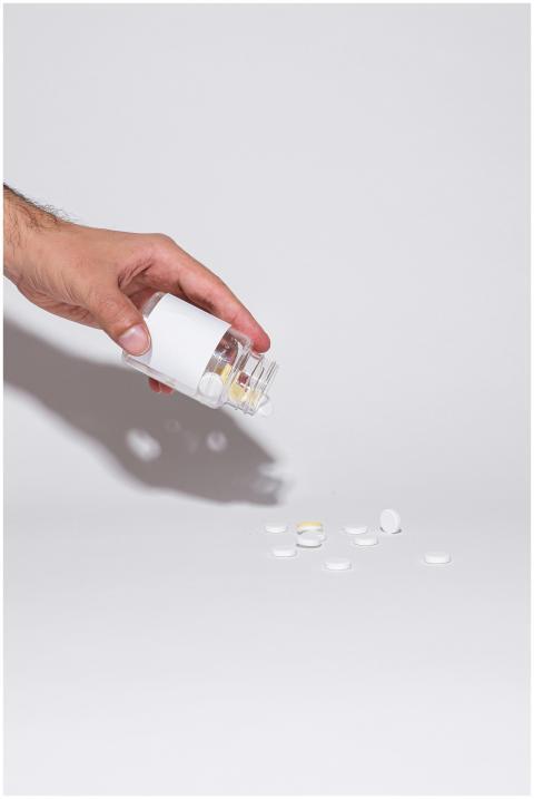 A hand holding a glass bottle pouring pills onto a