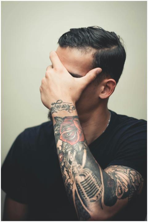 Stylish man with detailed arm tattoos covers face