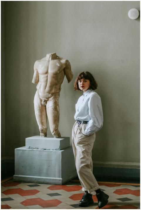Stylish woman poses beside a Greek sculpture in an