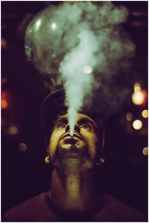 Low-angle portrait of a man vaping at night with a