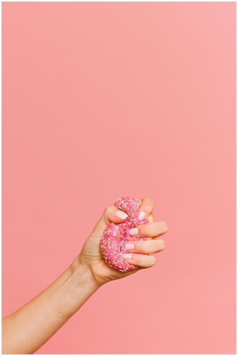 A hand with pink nails squeezes a donut with pink