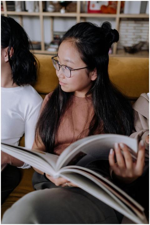 Teenage girl with glasses reading a book on a sofa