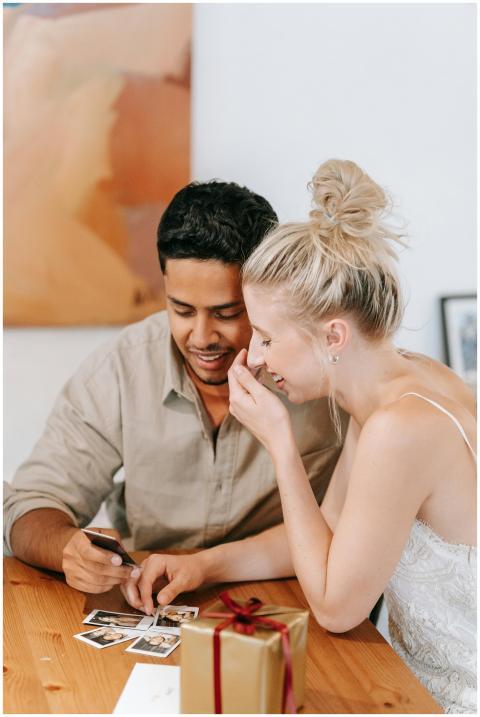 Happy couple sitting indoors and looking at Polaro