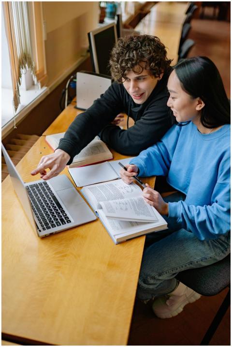 Two students working together on a laptop at a des