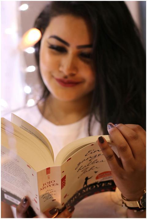 Smiling woman enjoying a book indoors, surrounded