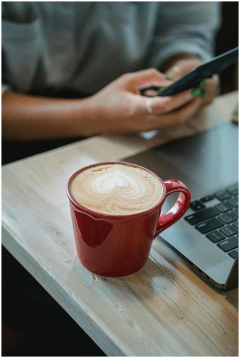 A red coffee cup with latte art sits on a table be