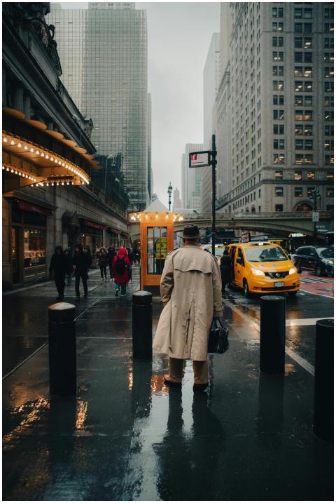 Man in trench coat on rainy NYC street with taxis
