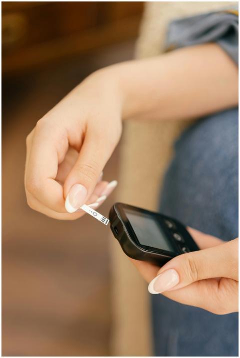 Hands holding a glucometer while inserting a test