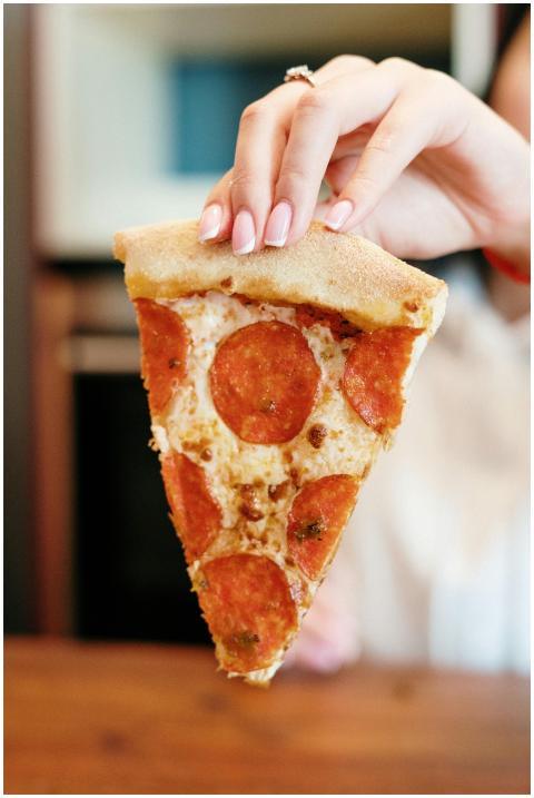 A hand with a polished manicure holds a pepperoni