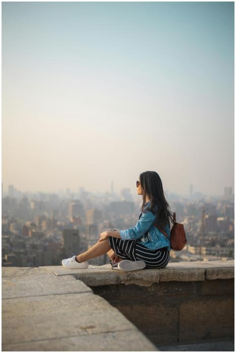 A young woman in casual attire sits on a rooftop t