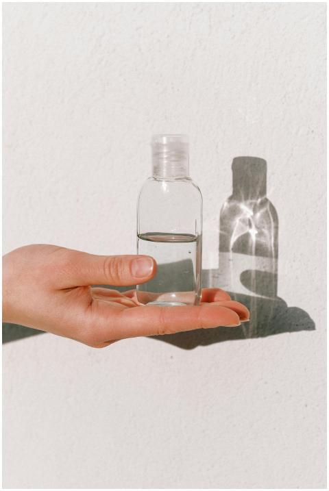 A hand holding a clear sanitizer bottle against a