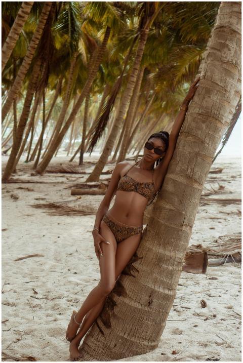 Elegant woman in bikini leaning against palm tree