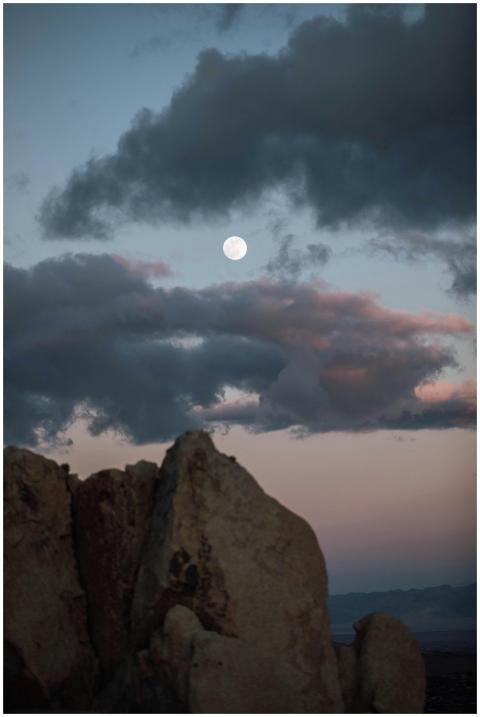 Full moon illuminates rocky formations under a dra
