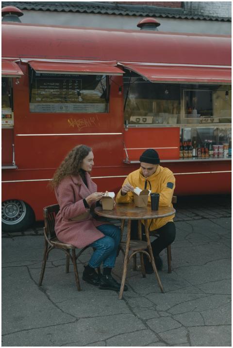 A couple enjoys takeout food at a table beside a r