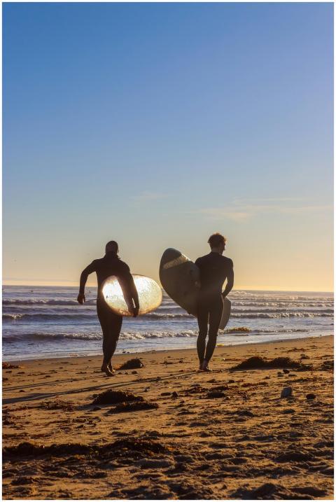 Two surfers walk along a sandy beach in Santa Barb