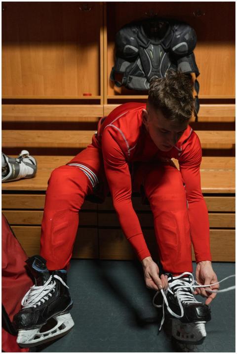 An ice hockey player in a red uniform lacing skate