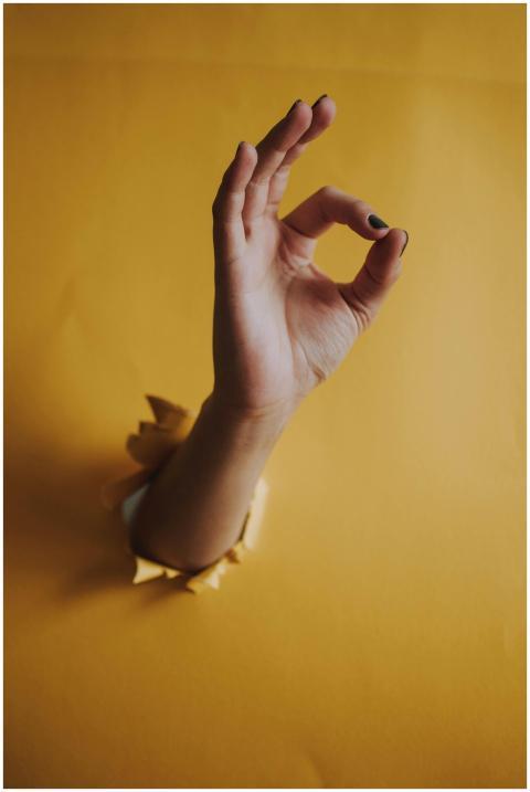 A hand pokes through yellow paper showing an OK ge