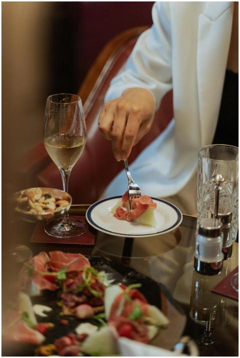 Person enjoying prosciutto and wine at an upscale