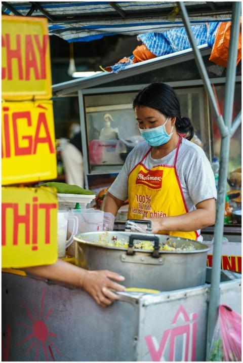 A street food vendor wearing a mask prepares a tra