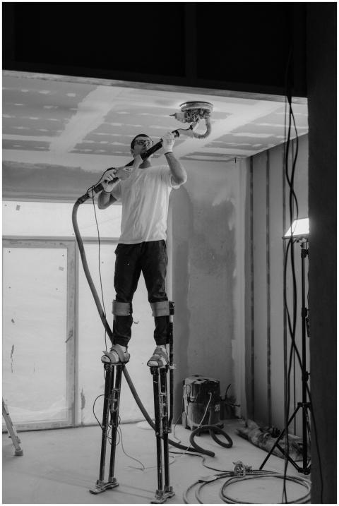 Worker using stilts and power sander on ceiling in