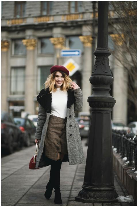 Stylish woman in coat and beret walking in city st