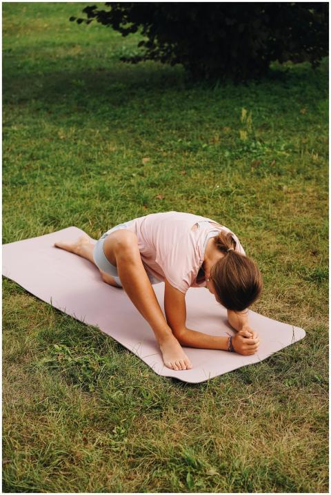 A woman performing yoga stretches on a mat in a gr