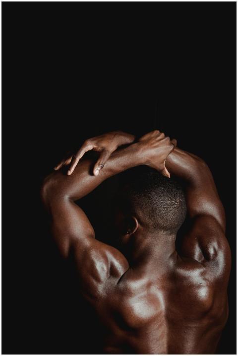 A muscular man flexing his back and arms against a