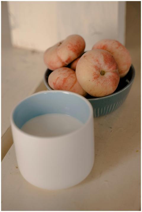 Bowl of fresh peaches with a cup of milk on a rust