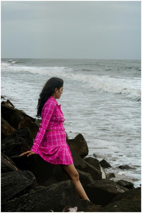 Woman in a vibrant pink dress sits on rocks by the